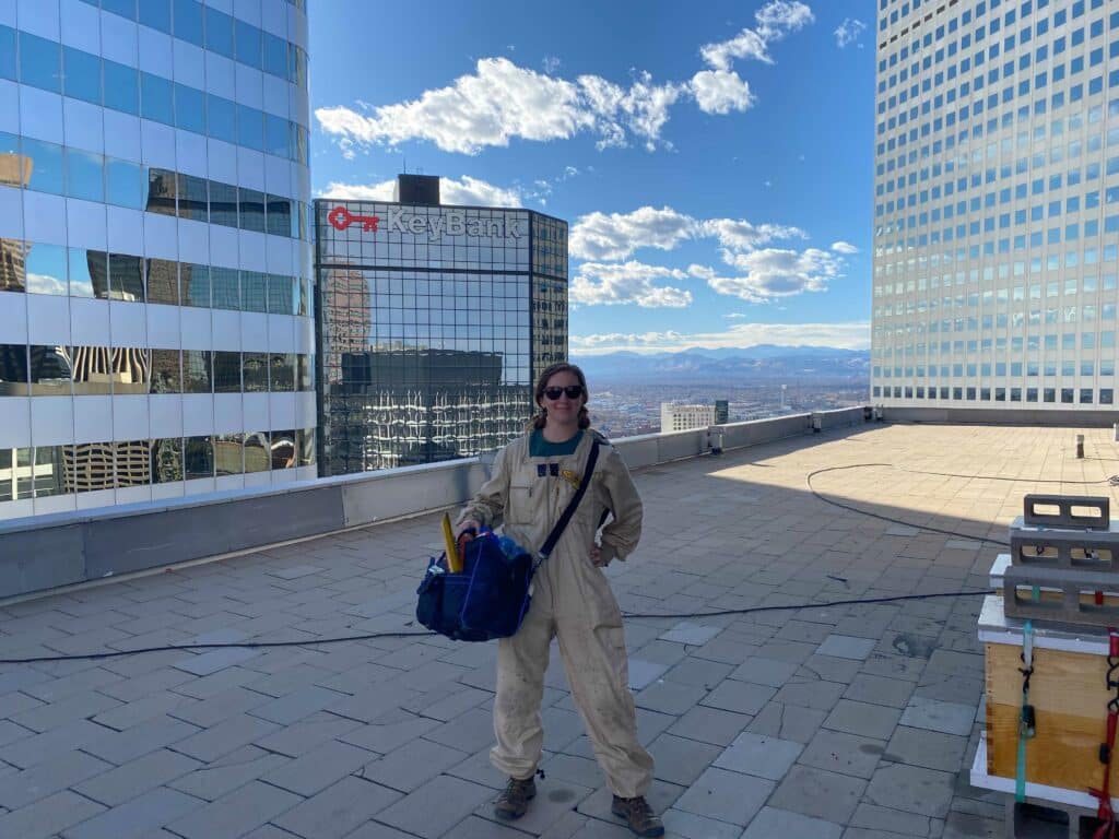 Denver beekeeper on a rooftop with the Rocky Mountains in the background
