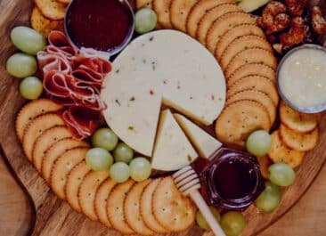 Honey, cheese, crackers, and grapes arranged on a wooden platter