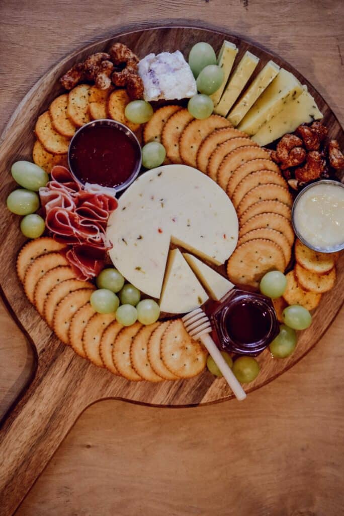 Honey, cheese, crackers, and grapes arranged on a wooden platter