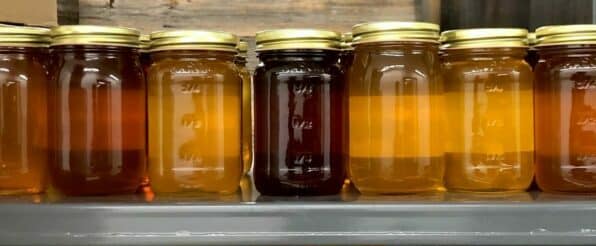 multi-colored jars of different types of honey sit in a row on a shelf