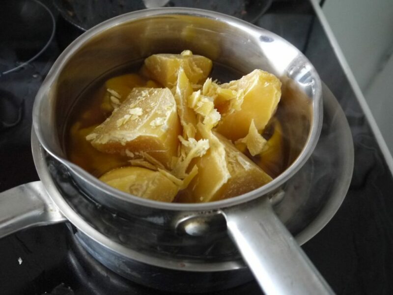 chunks of beeswax in a metal bowl in a larger pot of boiling water on the stove