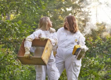 Best Bees beekeepers stand in front of greenery, holding hive tools and smiling at each other on a property with a FitWel certification