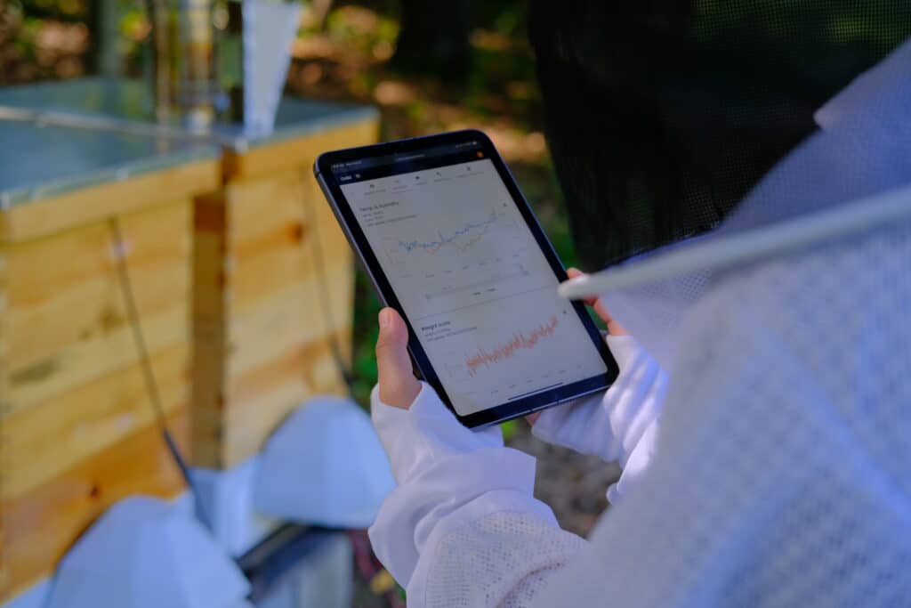 A beekeeper holds an iPad screen showing multiple data graphs