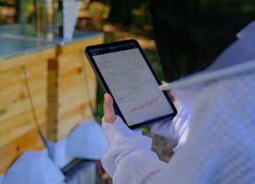 A beekeeper holds an iPad screen showing multiple data graphs