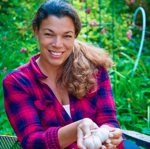 Renee Headshot smiling in a garden holding garlic