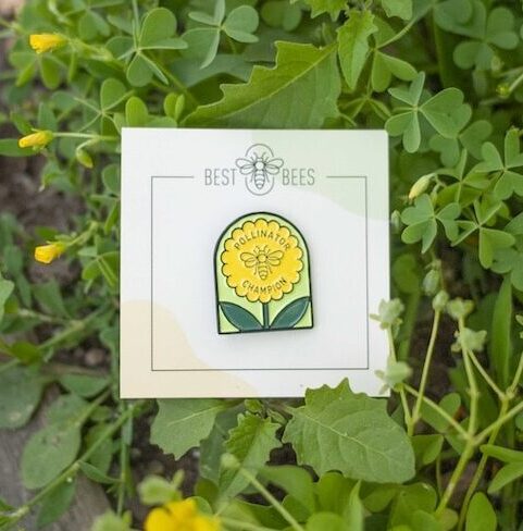 An enamel pin featuring a yellow flower on a white paper card